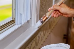 Closeup image of mans hand with paintbrush while painting window trim